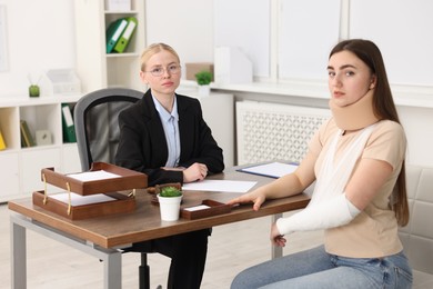 Photo of Injured woman and lawyer at table in office, selective focus