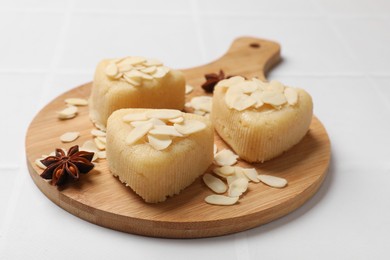 Photo of Pieces of delicious sweet semolina halva with almond flakes on white tiled table, closeup