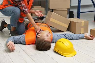 Photo of Accident at work. Woman checking pulse of her unconscious colleague in warehouse