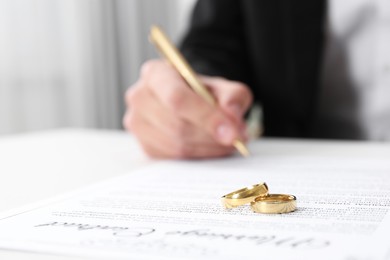 Photo of Man signing marriage contract and wedding rings on desk, selective focus