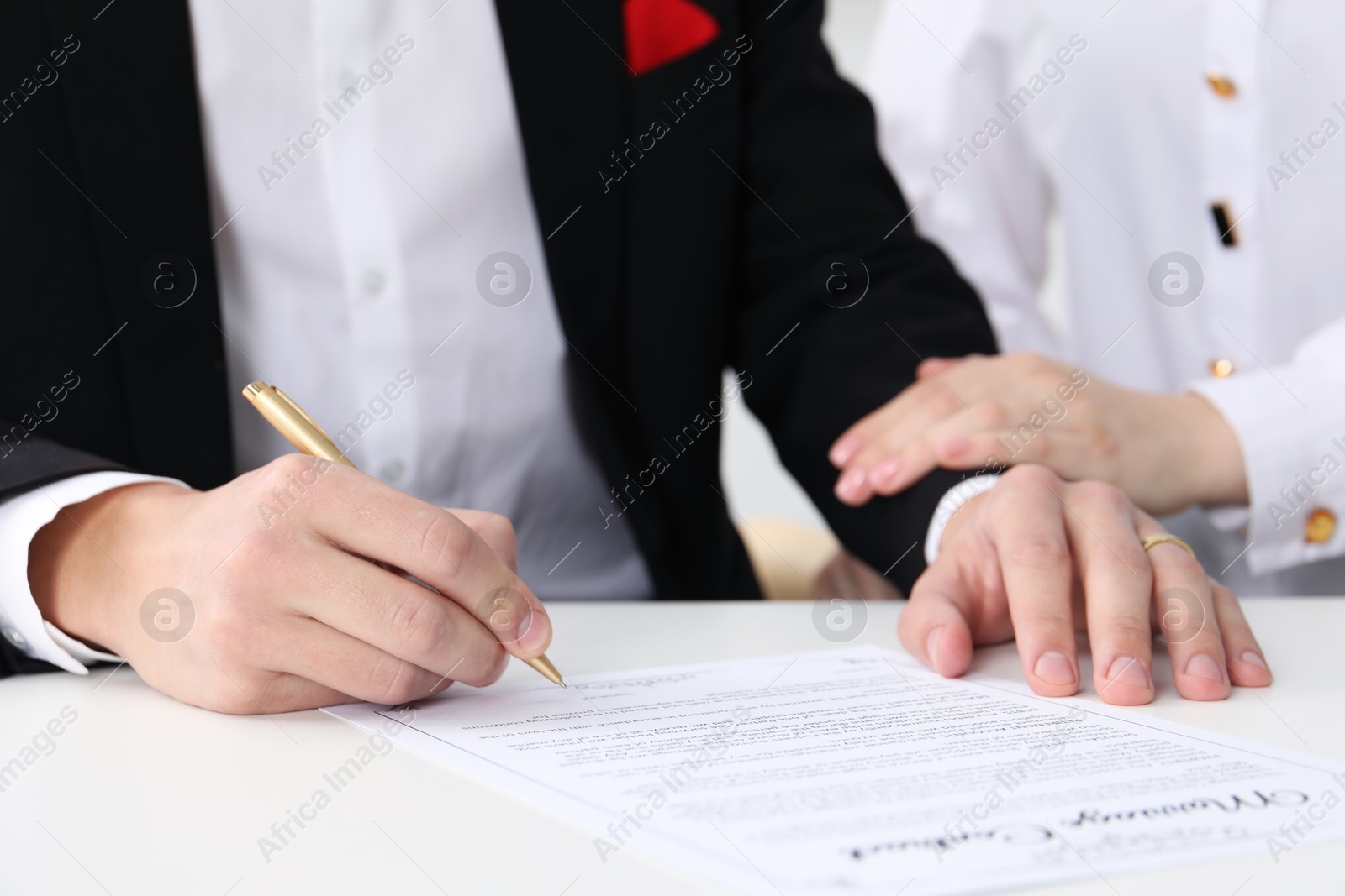 Photo of Newlyweds signing marriage contract at desk, closeup