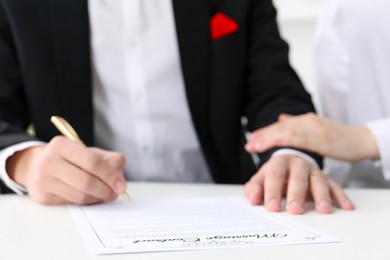 Photo of Newlyweds signing marriage contract at desk, closeup