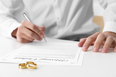 Photo of Man signing marriage contract and wedding rings on desk, selective focus