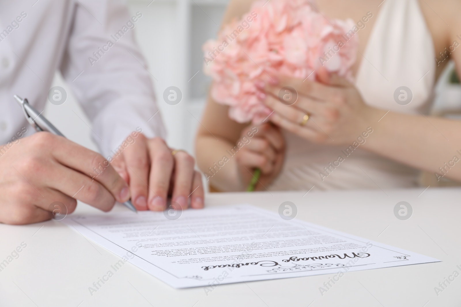 Photo of Newlyweds signing marriage contract at desk, closeup