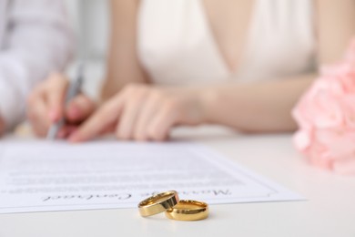 Photo of Woman signing marriage contract and wedding rings on desk, selective focus