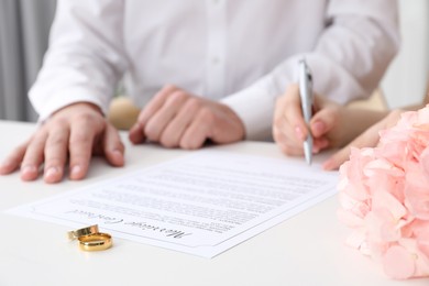 Photo of Newlyweds signing marriage contract and wedding rings on desk, selective focus