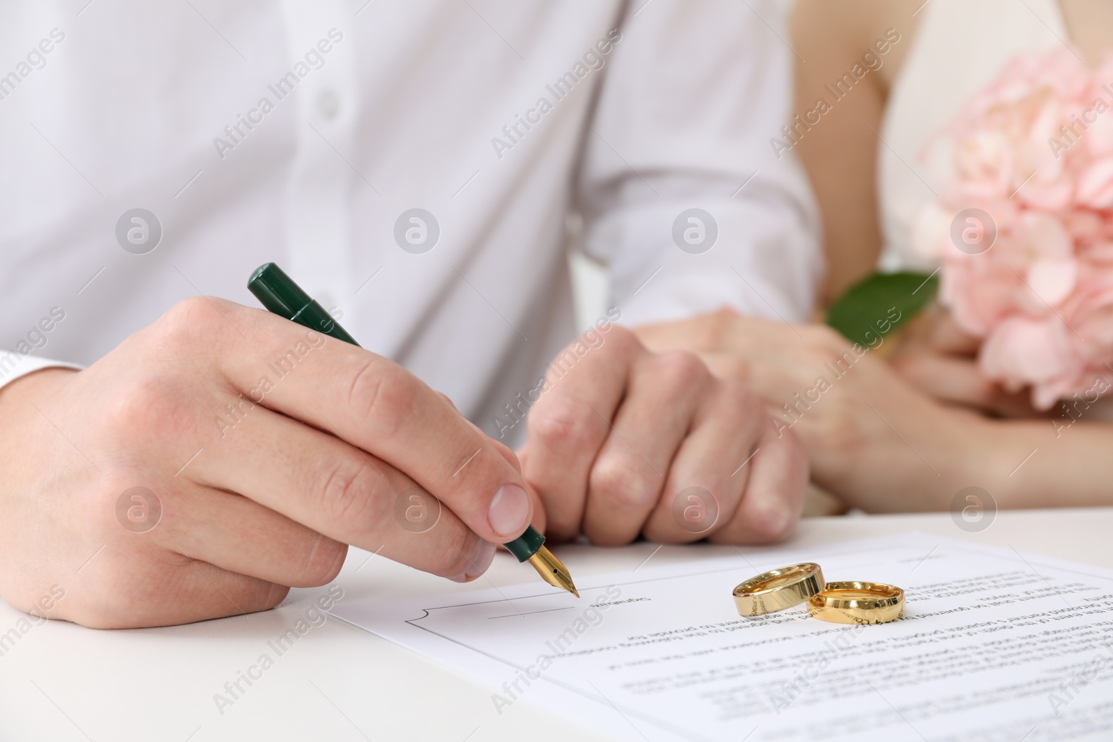 Photo of Newlyweds signing marriage contract and wedding rings on desk, selective focus