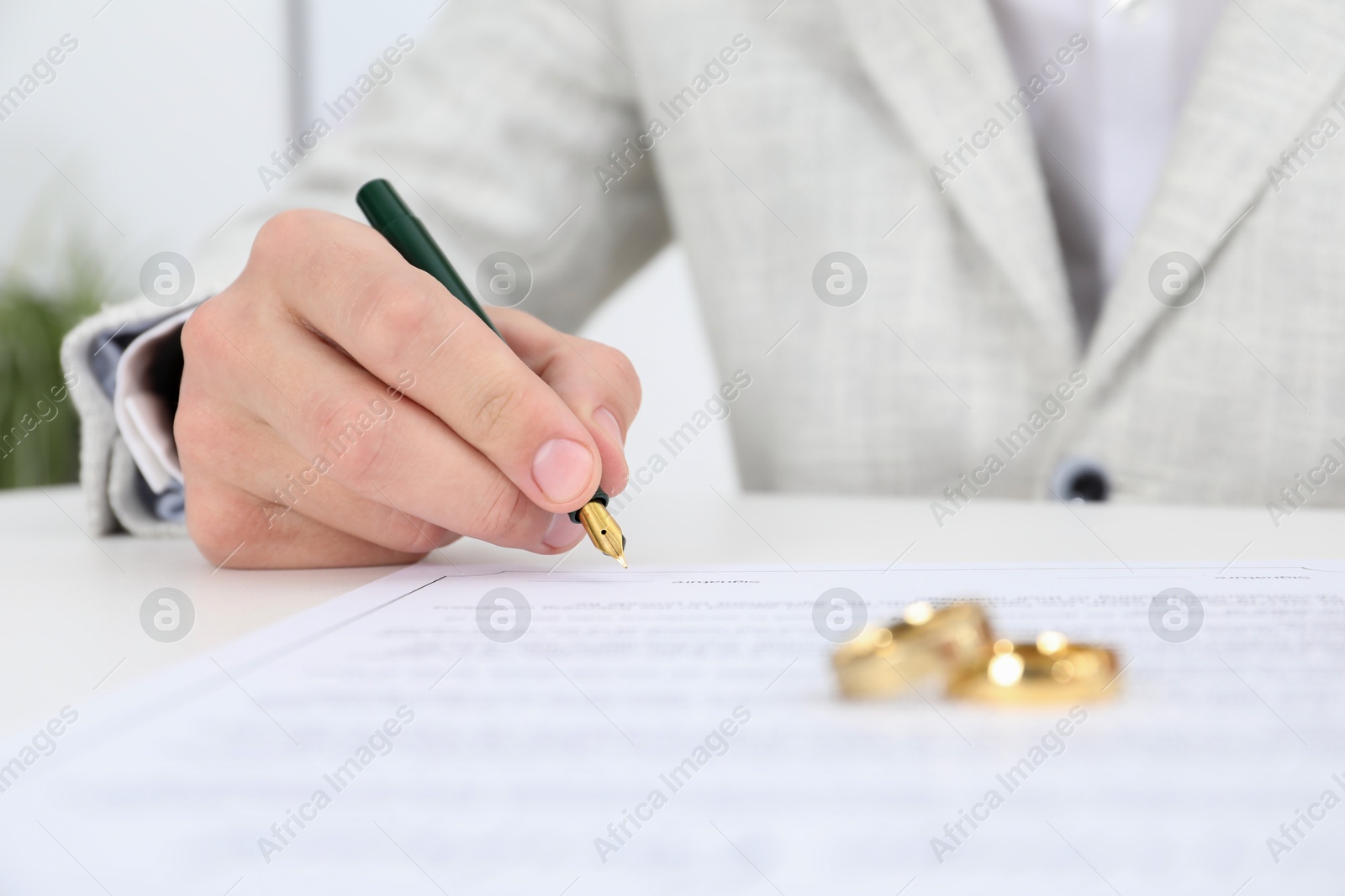 Photo of Man signing marriage contract and wedding rings on desk, selective focus