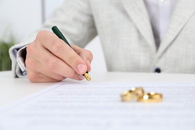 Photo of Man signing marriage contract and wedding rings on desk, selective focus