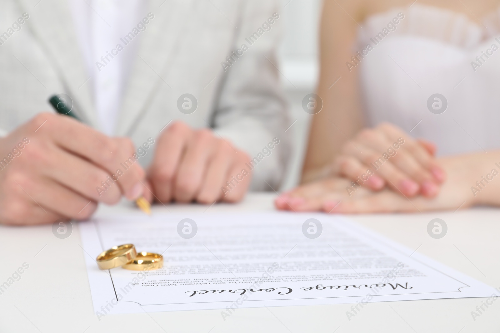 Photo of Newlyweds signing marriage contract and wedding rings on desk, selective focus