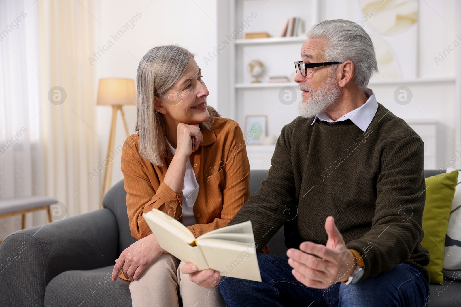 Photo of Cute elderly couple reading book together on sofa at home