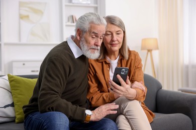 Photo of Cute elderly couple with smartphone on sofa at home