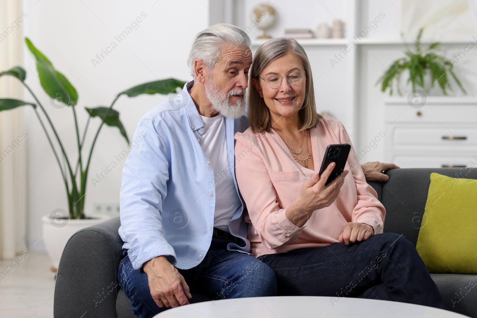 Photo of Happy elderly couple looking at smartphone on sofa at home