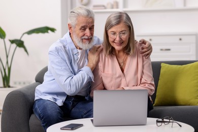 Photo of Happy elderly couple looking at laptop on sofa at home