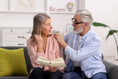 Photo of Cute elderly couple reading book together on sofa at home