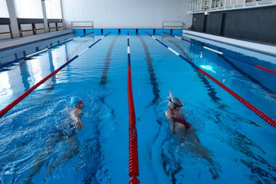 Photo of Young man and woman swimming in pool indoors