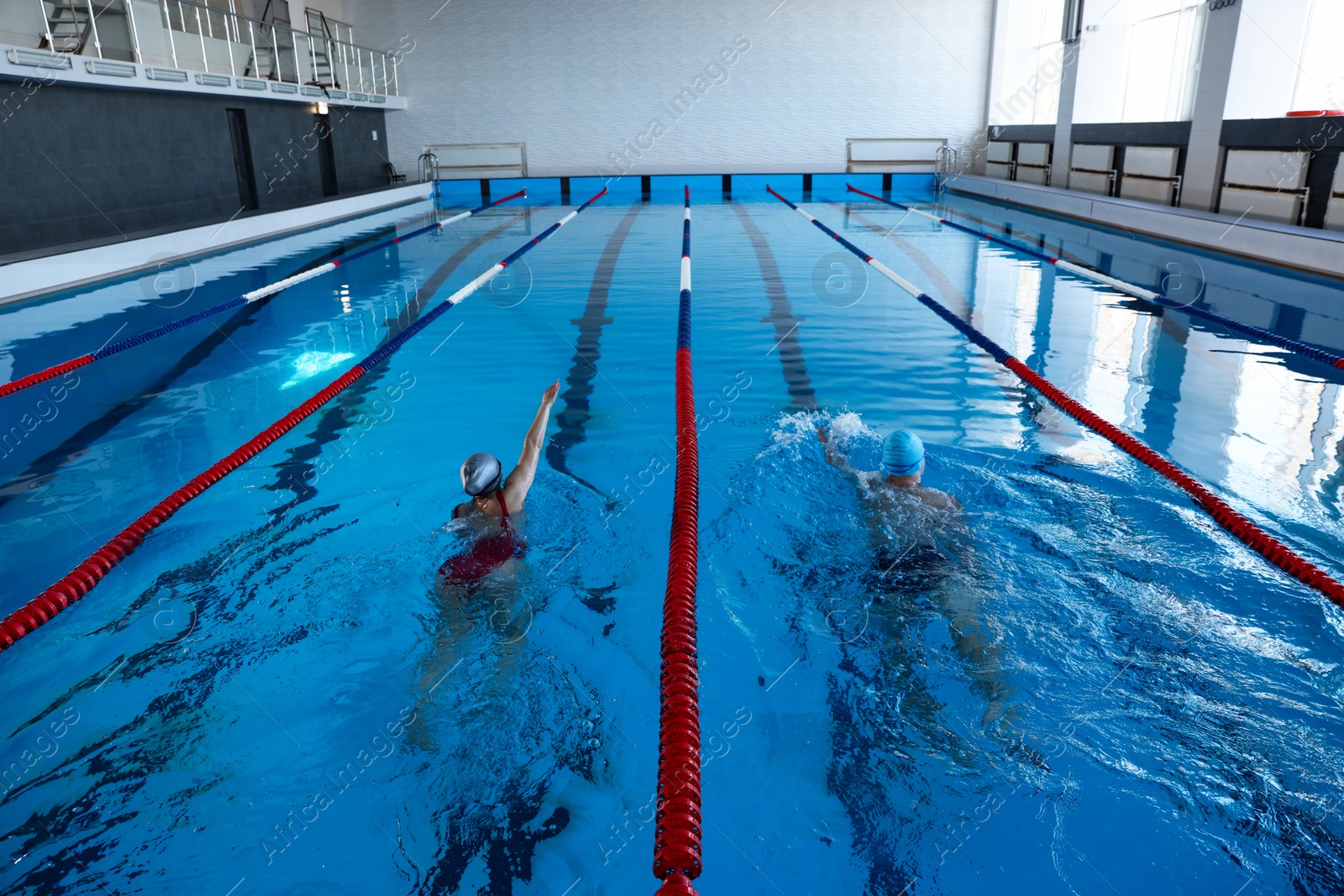 Photo of Young man and woman swimming in pool indoors