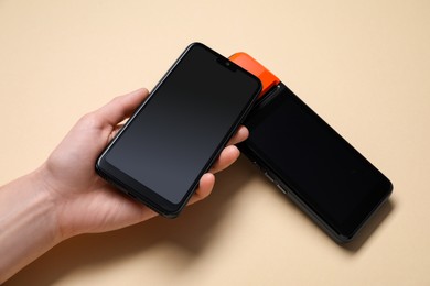 Photo of Woman with smartphone using payment terminal on beige background, above view