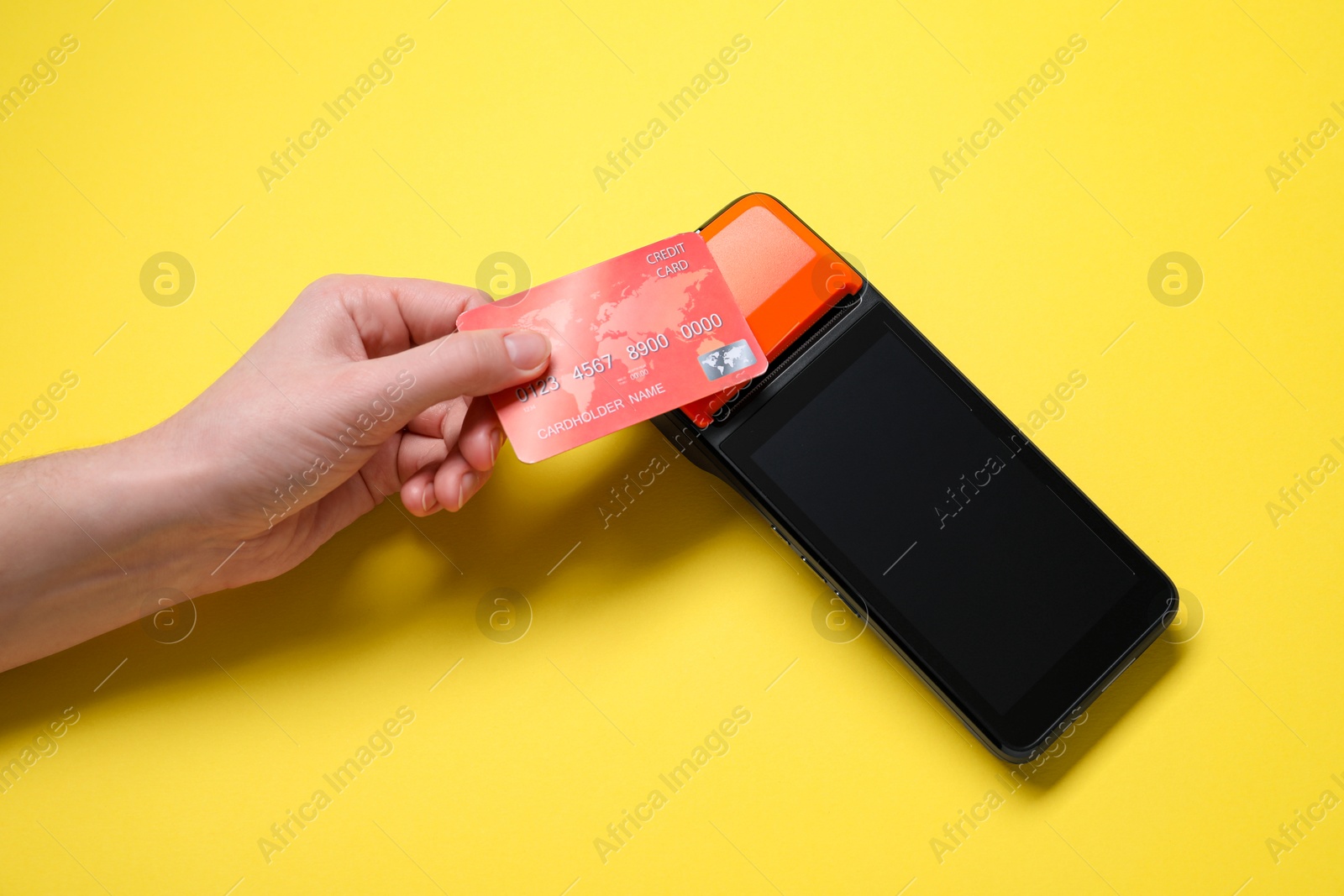 Photo of Woman with credit card using payment terminal on yellow background, top view