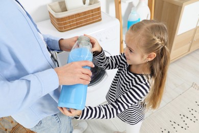 Photo of Little girl with detergent helping her mom doing laundry at home