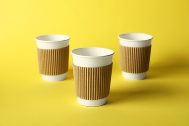 Photo of Paper cups on yellow background, selective focus. Mockup for design