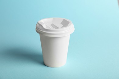 Photo of One paper cup on light blue background. Mockup for design