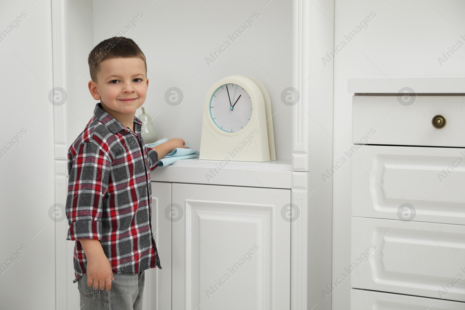 Photo of Little helper. Cute boy wiping dust from chest of drawers at home