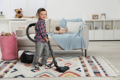 Photo of Little helper. Cute boy vacuuming at home