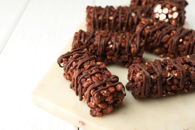 Photo of Delicious chocolate puffed rice bars on white wooden table, closeup. Space for text