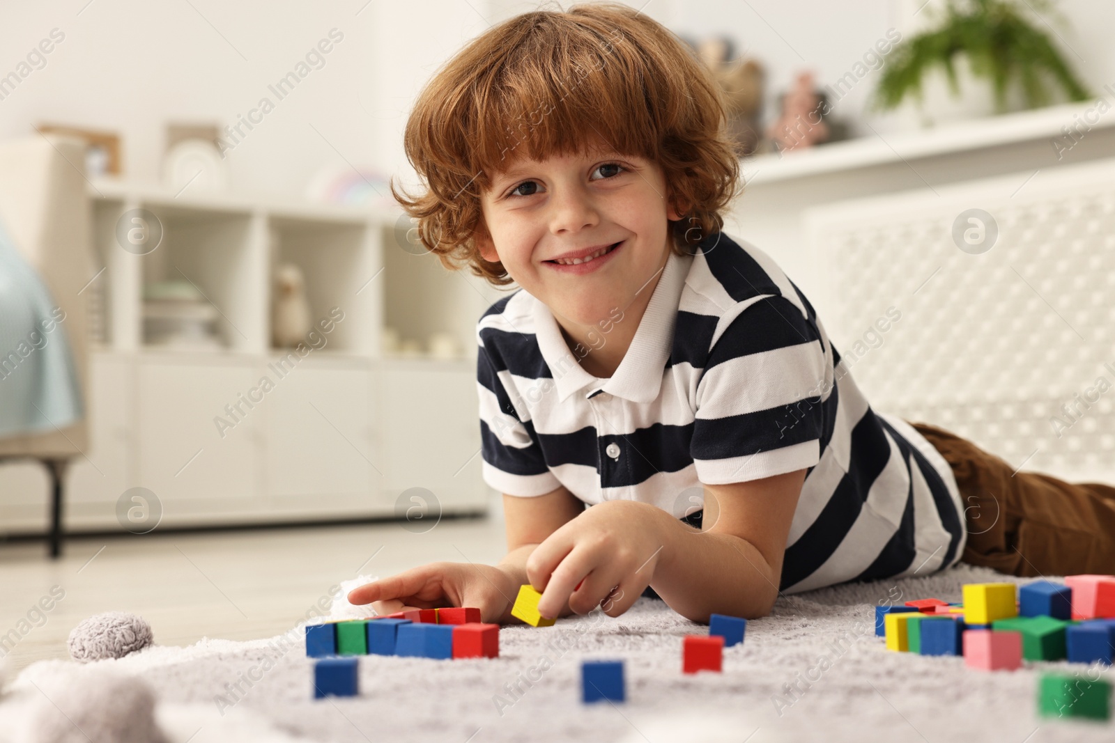 Photo of Little boy playing with colorful cubes on floor at home