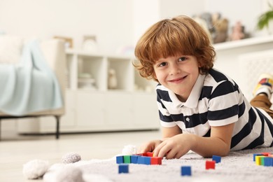 Photo of Little boy playing with colorful cubes on floor at home, space for text