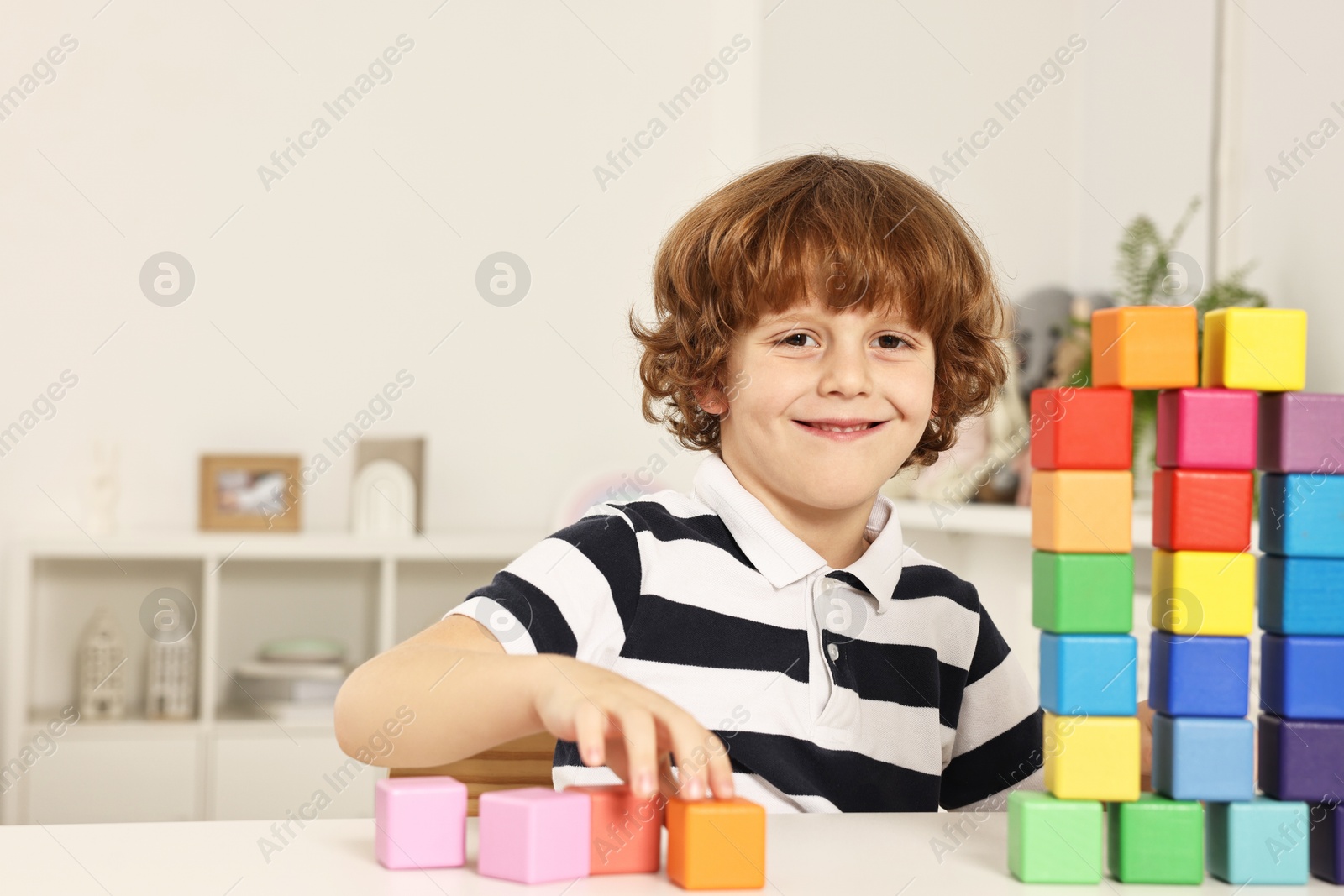 Photo of Little boy stacking colorful cubes at white table indoors, space for text