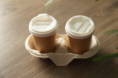Photo of Holder with paper cups on wooden table, closeup. Mockup for design