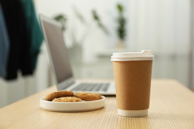Photo of Paper cup, plate with cookies and laptop on wooden table indoors, closeup. Mockup for design