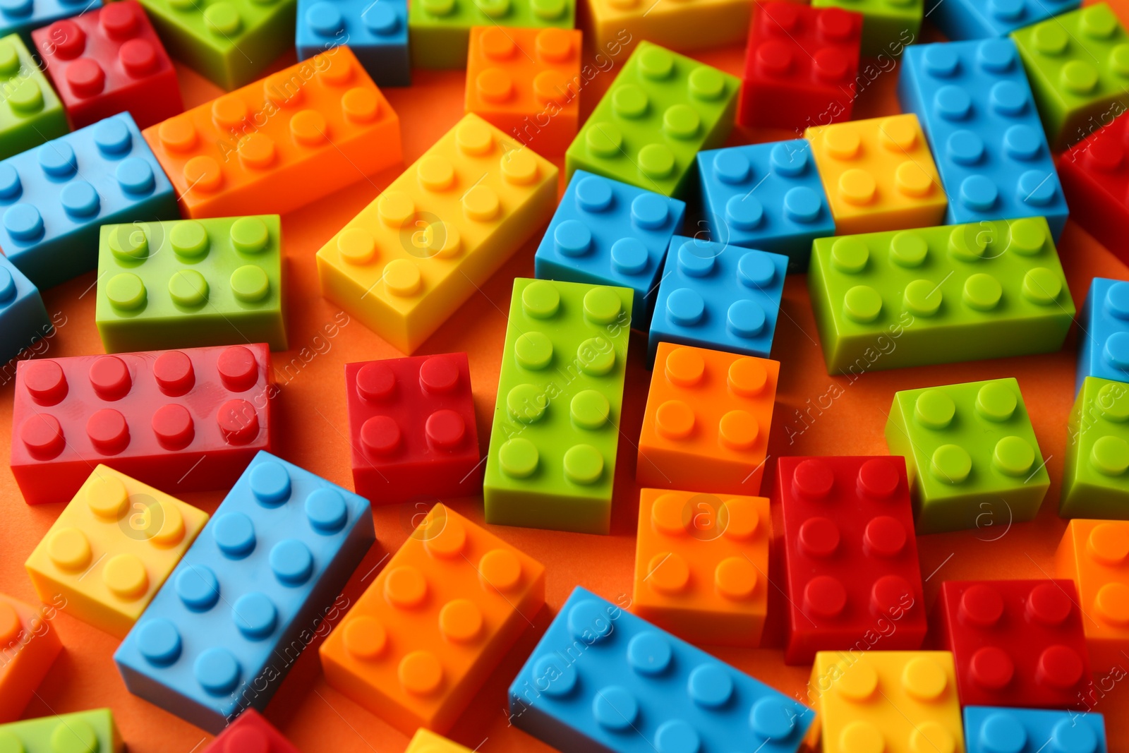 Photo of Construction toy. Colorful building bricks on orange background, closeup