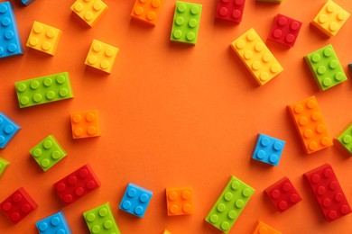 Photo of Frame of colorful building bricks on orange background, flat lay with space for text. Construction toy