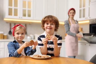 Photo of Happy kids eating tasty cookies while their mother baking in kitchen, selective focus