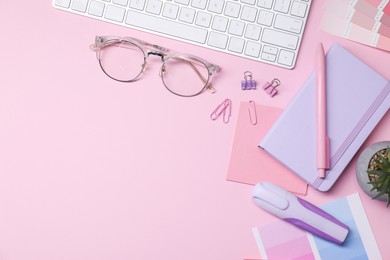 Photo of Designer's workplace with keyboard and stationery on pink background, flat lay. Space for text