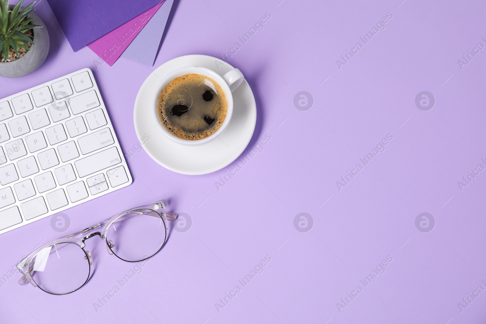 Photo of Designer's workplace with keyboard, stationery and cup of coffee on lilac background, flat lay. Space for text