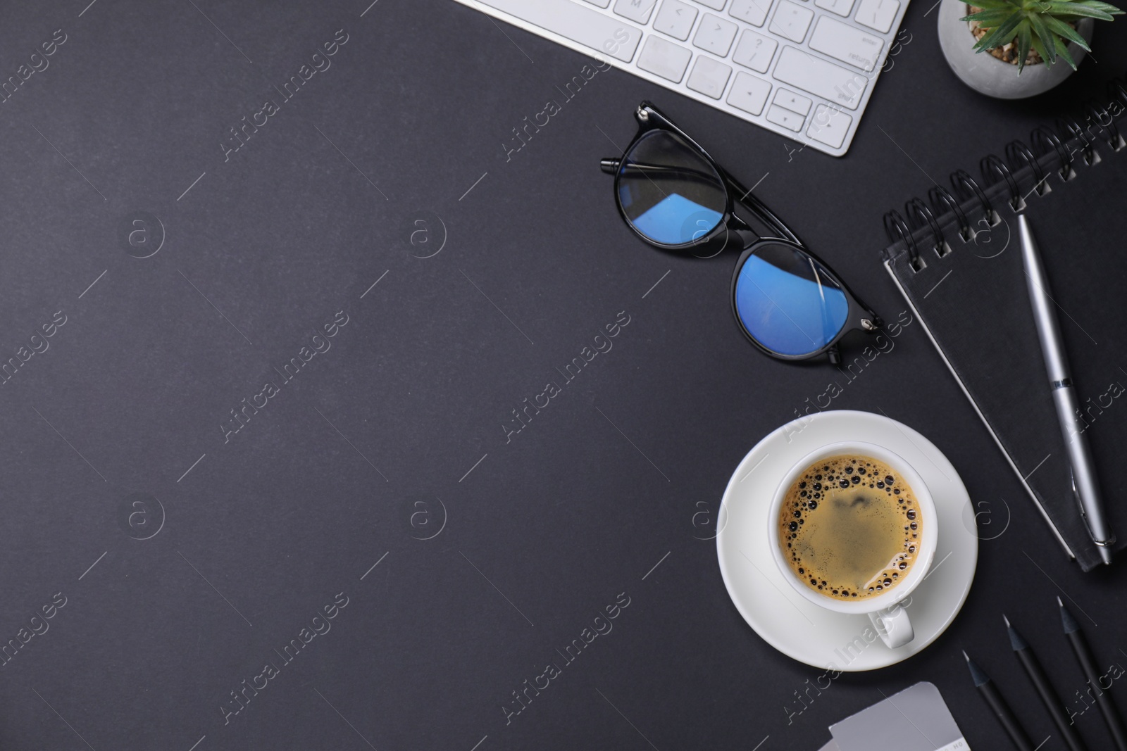 Photo of Designer's workplace with keyboard, stationery and cup of coffee on black background, flat lay. Space for text