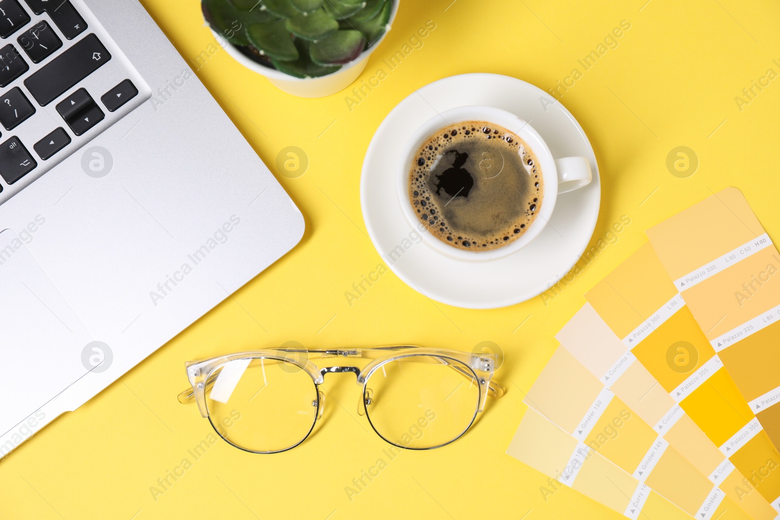 Photo of Designer's workplace with laptop, stationery and cup of coffee on yellow background, flat lay