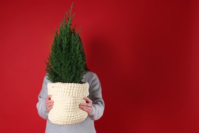 Photo of Woman with potted juniper tree on red background, space for text. Christmas decor