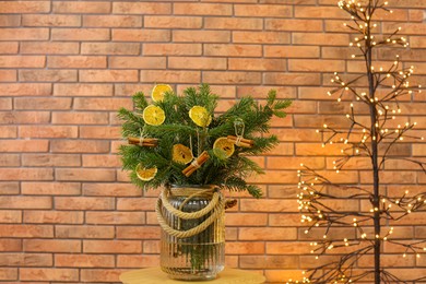 Photo of Beautiful fir tree branches decorated with dried orange slices and cinnamon sticks on table near Christmas tree lights