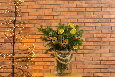 Photo of Beautiful fir tree branches decorated with dried orange slices and cinnamon sticks on table near Christmas tree lights