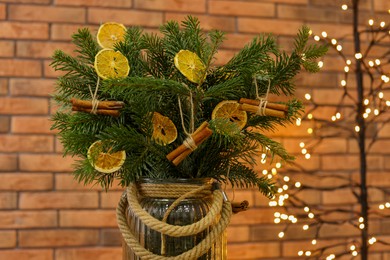 Photo of Beautiful fir tree branches decorated with dried orange slices and cinnamon sticks in vase against Christmas lights