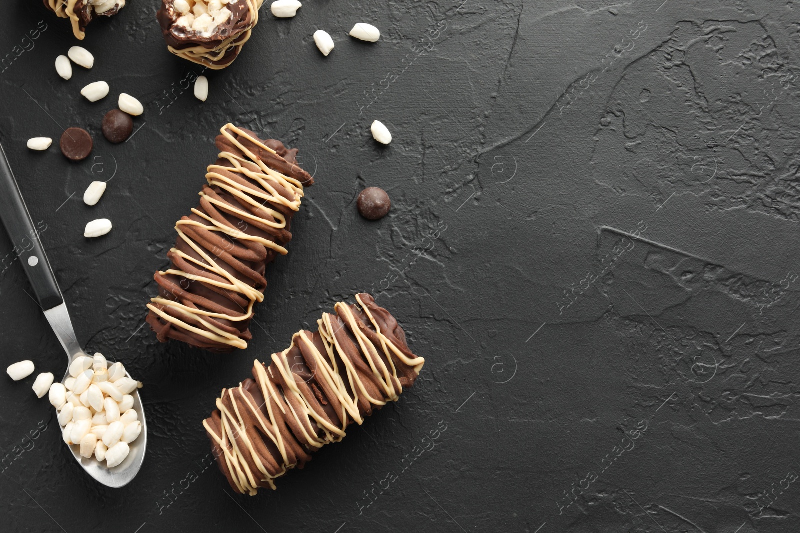 Photo of Delicious chocolate puffed rice bars and spoon on dark gray textured table, flat lay. Space for text