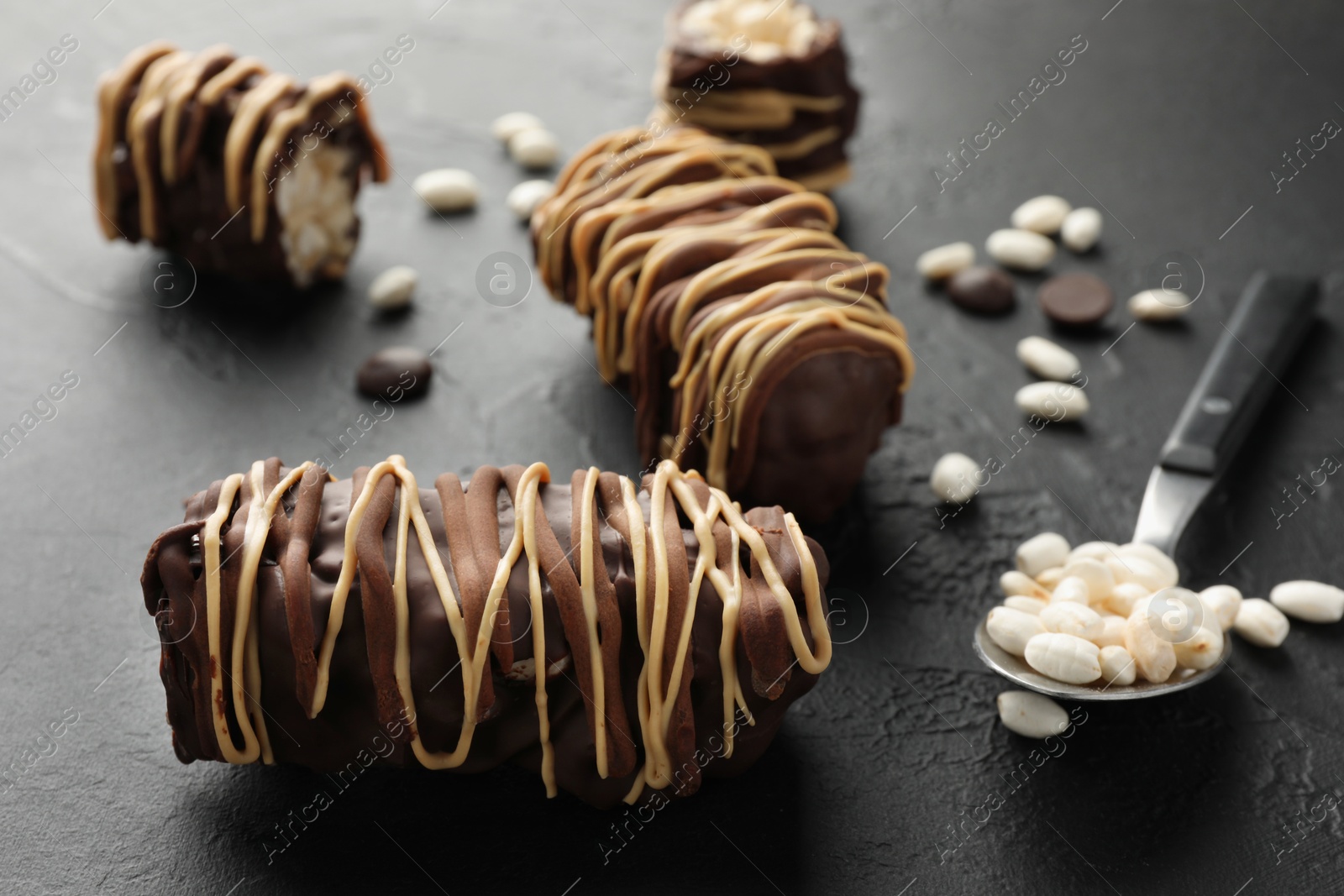 Photo of Delicious chocolate puffed rice bars and spoon on dark gray textured table, closeup