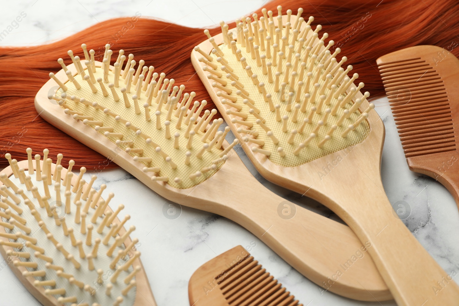 Photo of Set of different wooden brushes, combs and lock of hair on white marble table, closeup