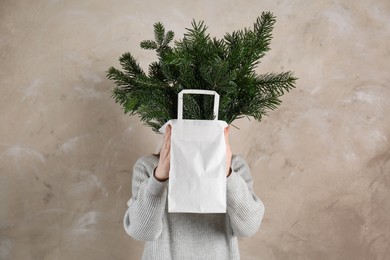 Photo of Woman holding green fir branches in paper bag near gray wall. Christmas decor