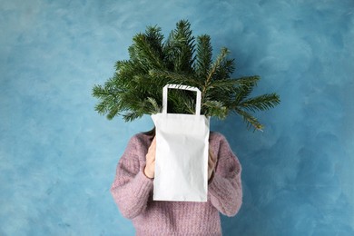 Photo of Woman holding green fir branches in paper bag near blue wall. Christmas decor